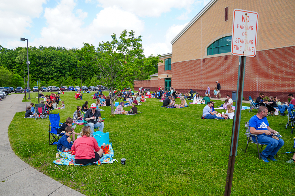 Dozens of Meadowview families spread out across the grass outside the school building during Lunch on the Lawn. Families sit on blankets and folding chairs while eating lunch together outdoors.