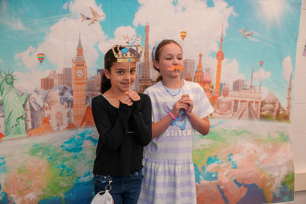 Two students in front of a backdrop holding funny looking mustaches