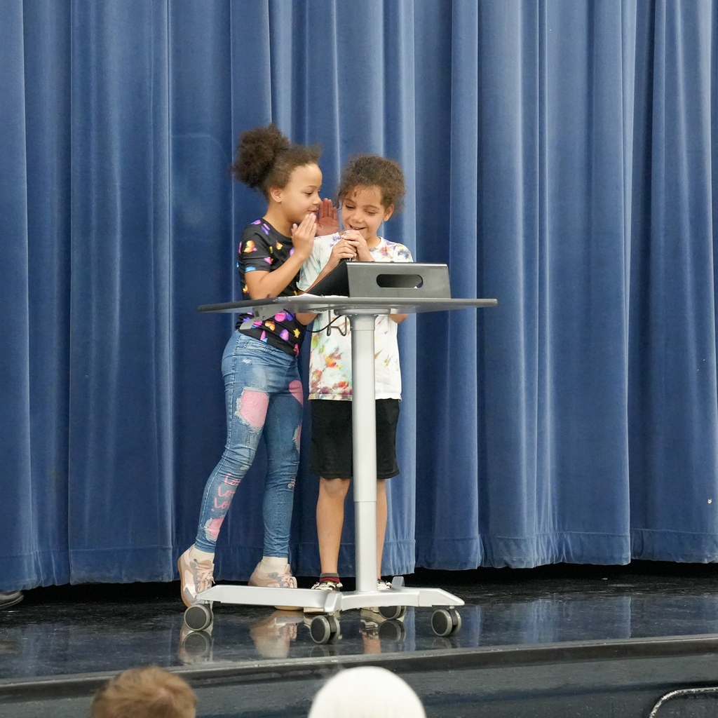 Two young students share a microphone on stage while reading poetry together during the Mulberry “Poet-Tea” event.