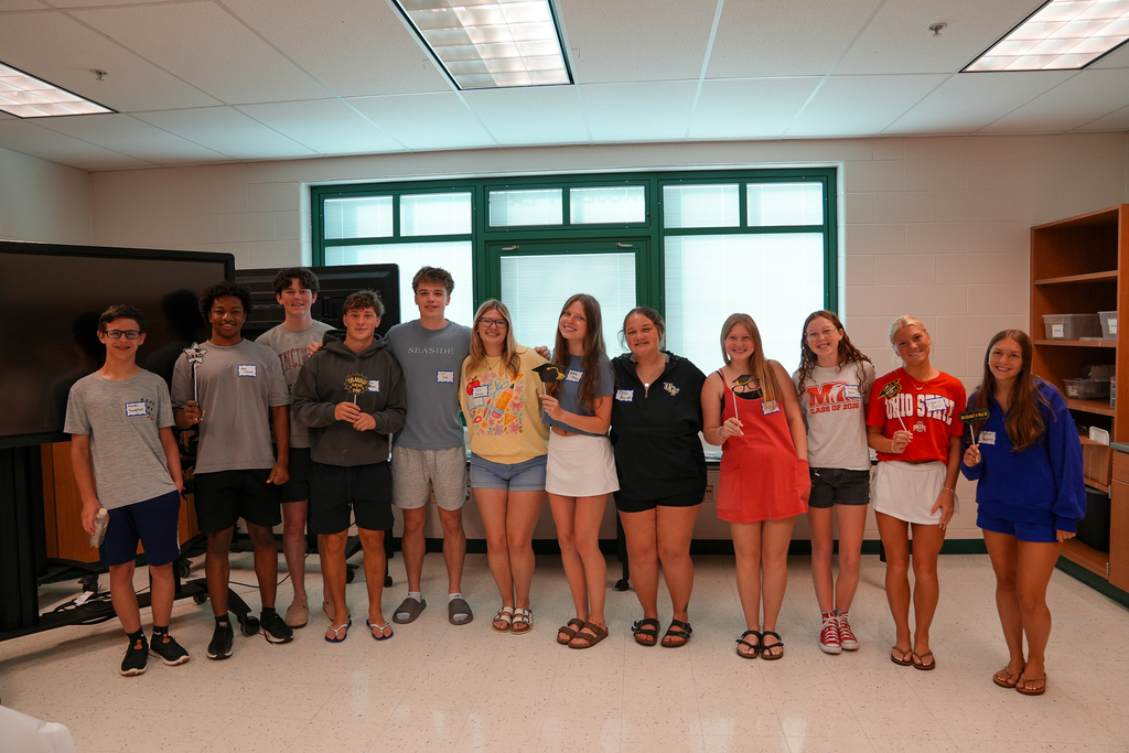 A group of graduating seniors stand together smiling and holding graduation-themed props during the Mulberry senior breakfast event.