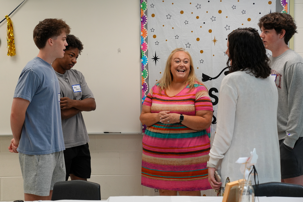 Mulberry staff members and graduating seniors stand together chatting and smiling during a senior breakfast celebration inside a classroom decorated for graduation.