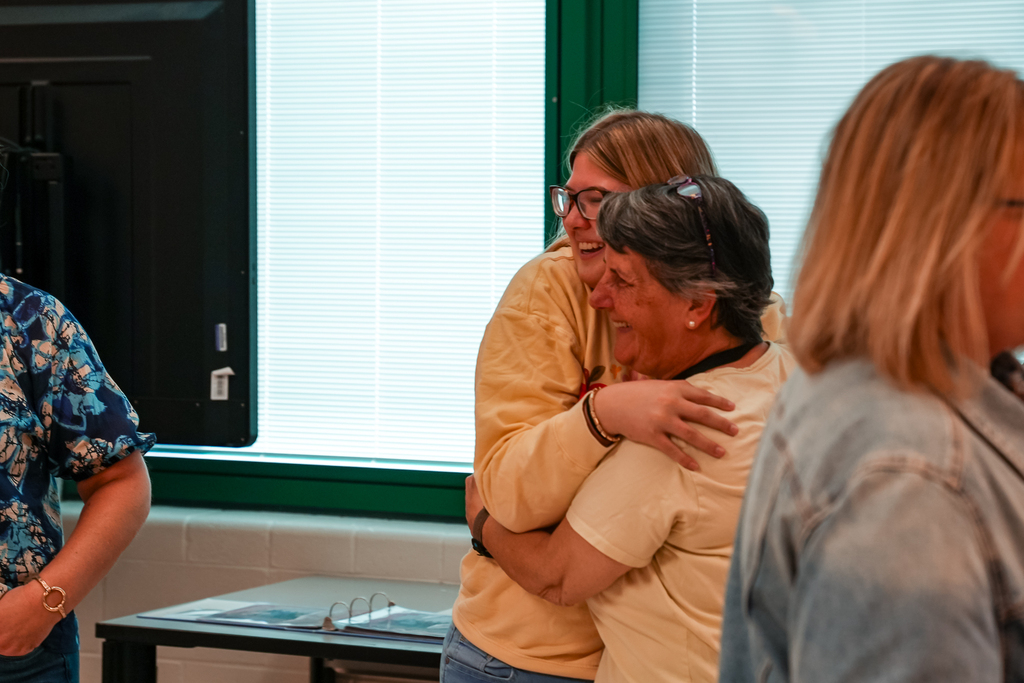 A former Mulberry student shares a hug with a staff member during the senior breakfast celebration as others mingle nearby.