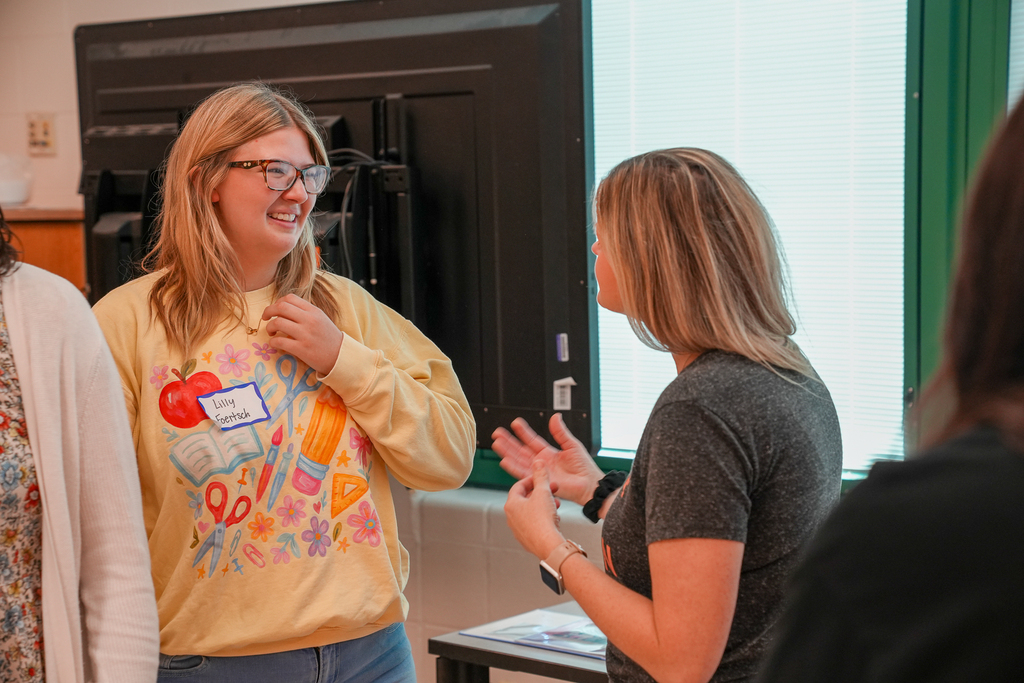 A graduating senior wearing a yellow sweatshirt speaks with Mulberry staff members during the breakfast celebration.