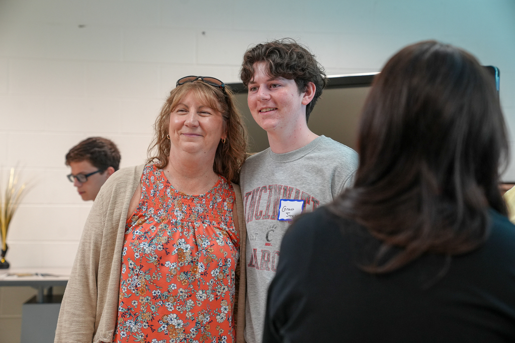 A Mulberry staff member poses for a photo with a graduating senior during the celebration as another student sits nearby in the background.