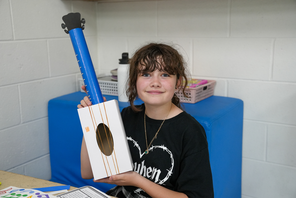 A student proudly holds up a handmade cardboard guitar project during a STEAM activity.
