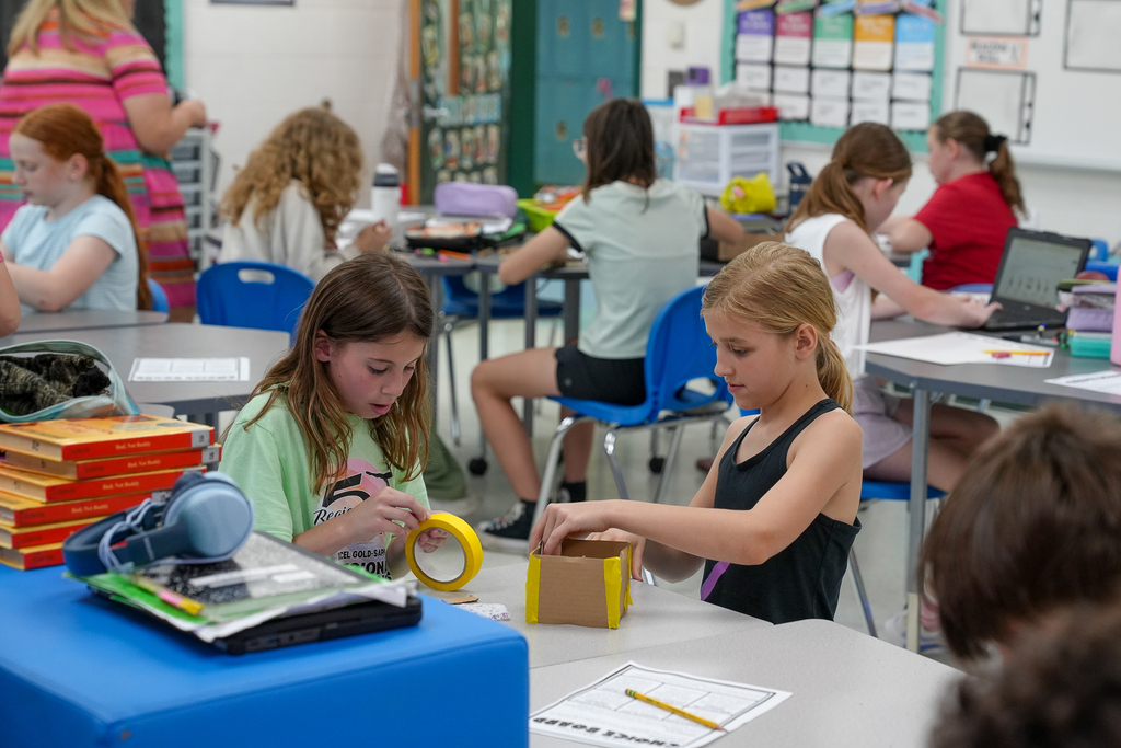 Two elementary students work together using tape and cardboard to build a small project during a classroom STEAM lesson.