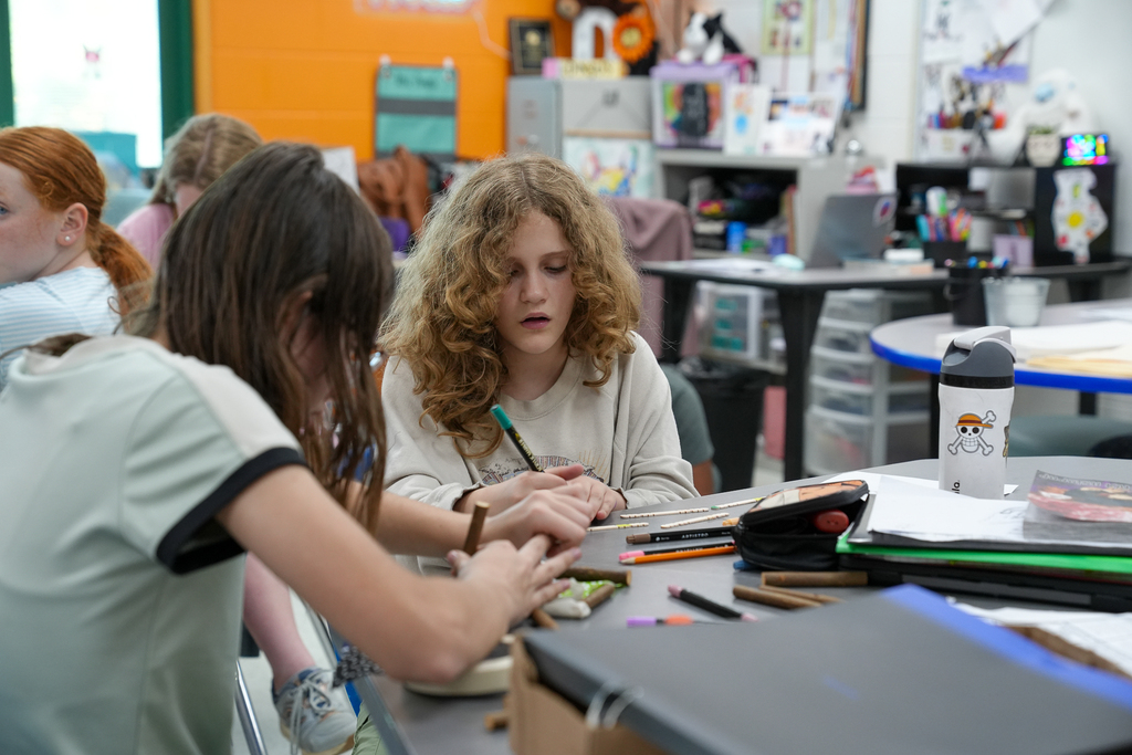 Students collaborate at a classroom table using colored pencils and craft materials during a hands-on STEAM activity.