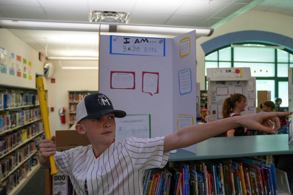 A student dressed as Babe Ruth poses with a baseball bat in front of a presentation board during Meadowview Elementary’s Wax Museum event in the school library.
