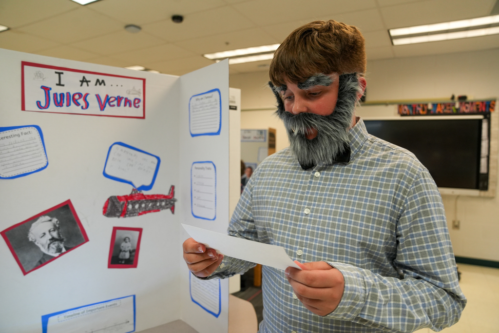 A student dressed as Jules Verne reads from a note card while standing beside a historical display board during Meadowview Elementary’s Wax Museum.