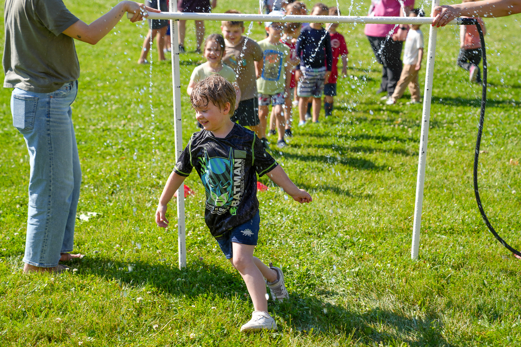 preschool student with blonde hair running through a sprinkler