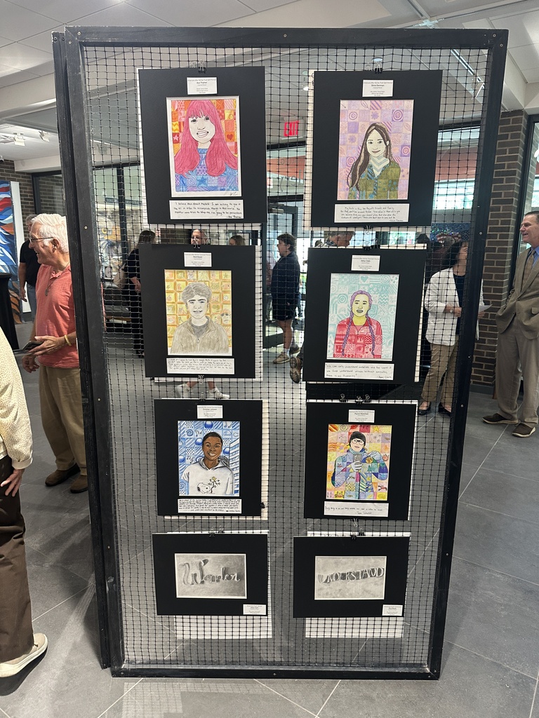 A large student art gallery panel featuring colorful portrait illustrations, typography artwork, and artist statements displayed during the showcase event as visitors walk through the exhibit space.