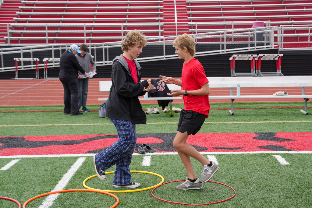 Two middle school students play rock-paper-scissors while standing inside colored hoops on the football field during field day games.
