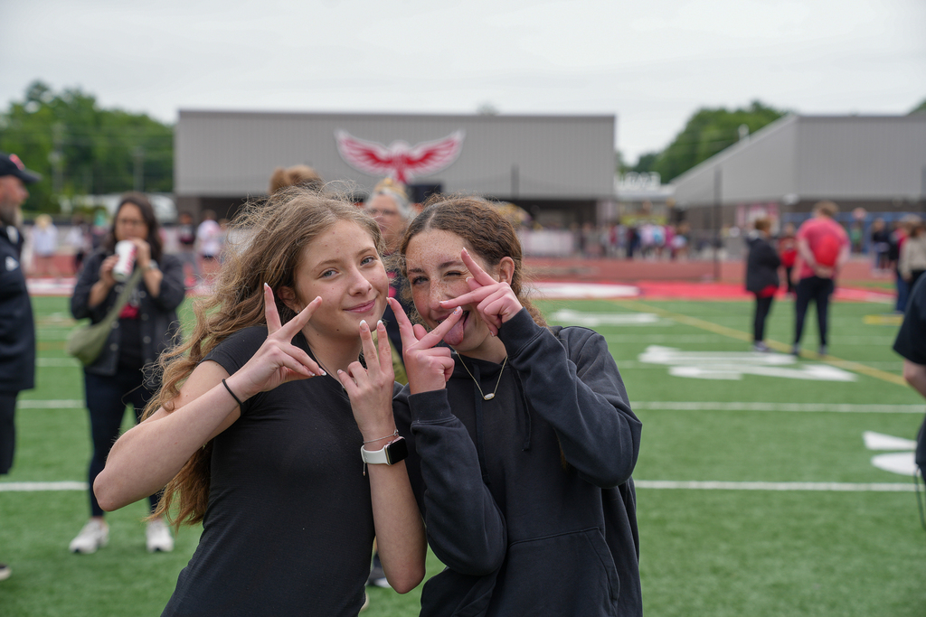 Two middle school students smile and pose together on the football field during field day activities.
