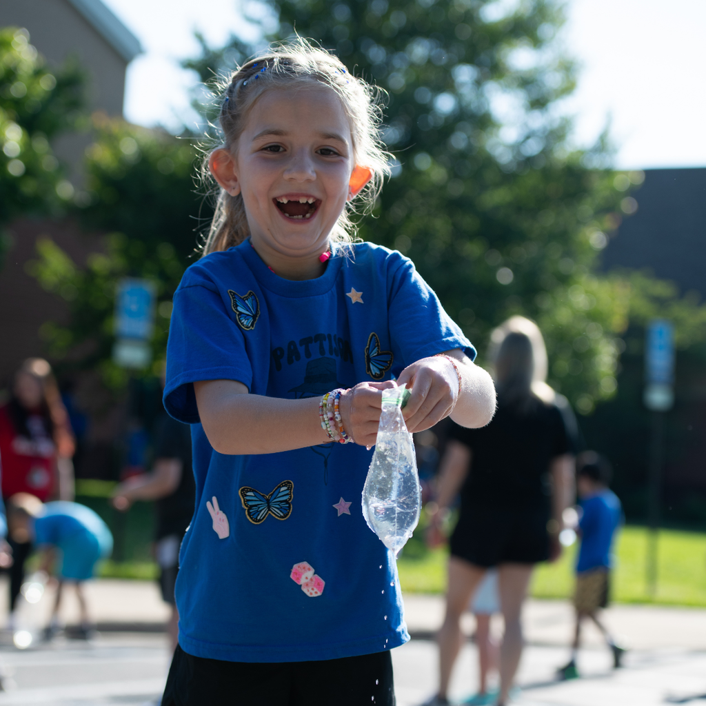 Another photo shows a young student in a blue Pattison Elementary shirt smiling while holding a water balloon as water drips from it.