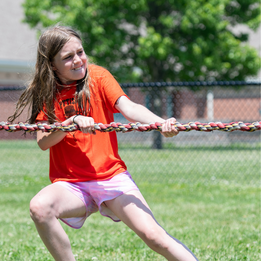 Another student in an orange shirt grips a rope tightly during a tug-of-war competition, concentrating as she pulls against the opposing team.