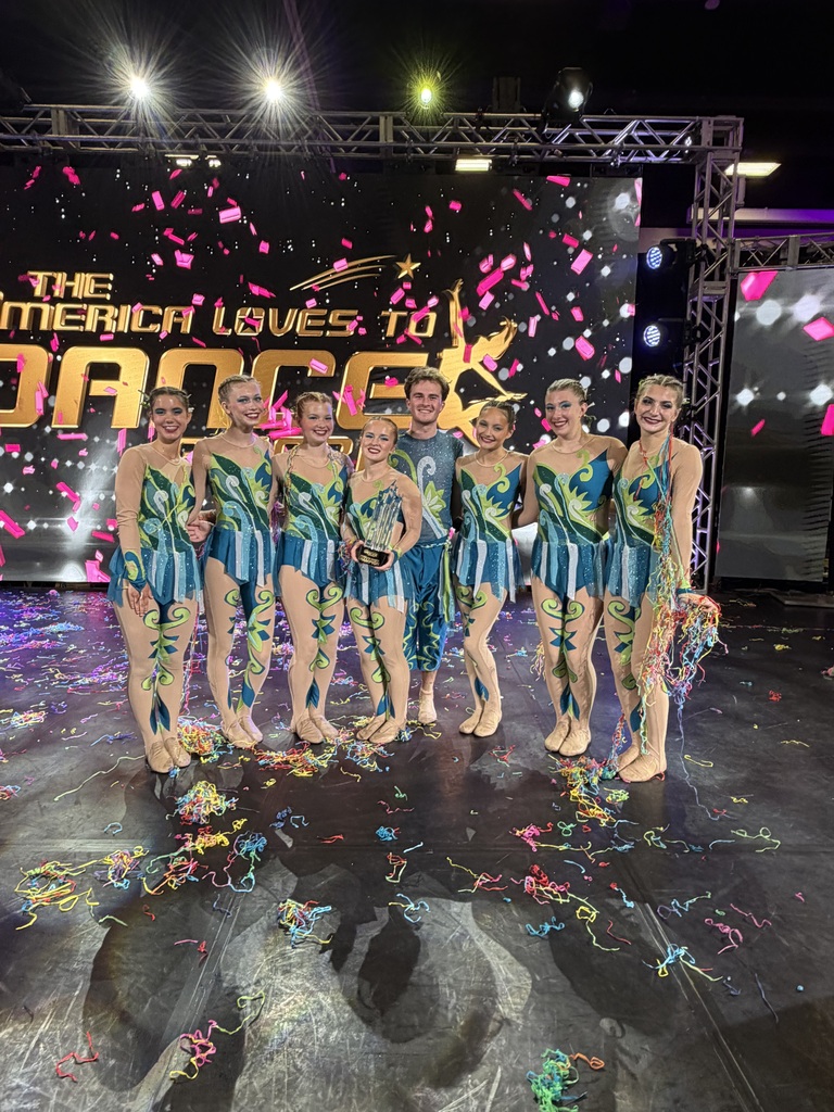 eight dancers pose together on stage holding their championship trophy. Streamers and confetti cover the floor around them, and a large Showstoppers Dance Competition backdrop is visible behind the group. The students smile proudly as they celebrate earning the Northern Finals Championship in the Senior Large Group category.