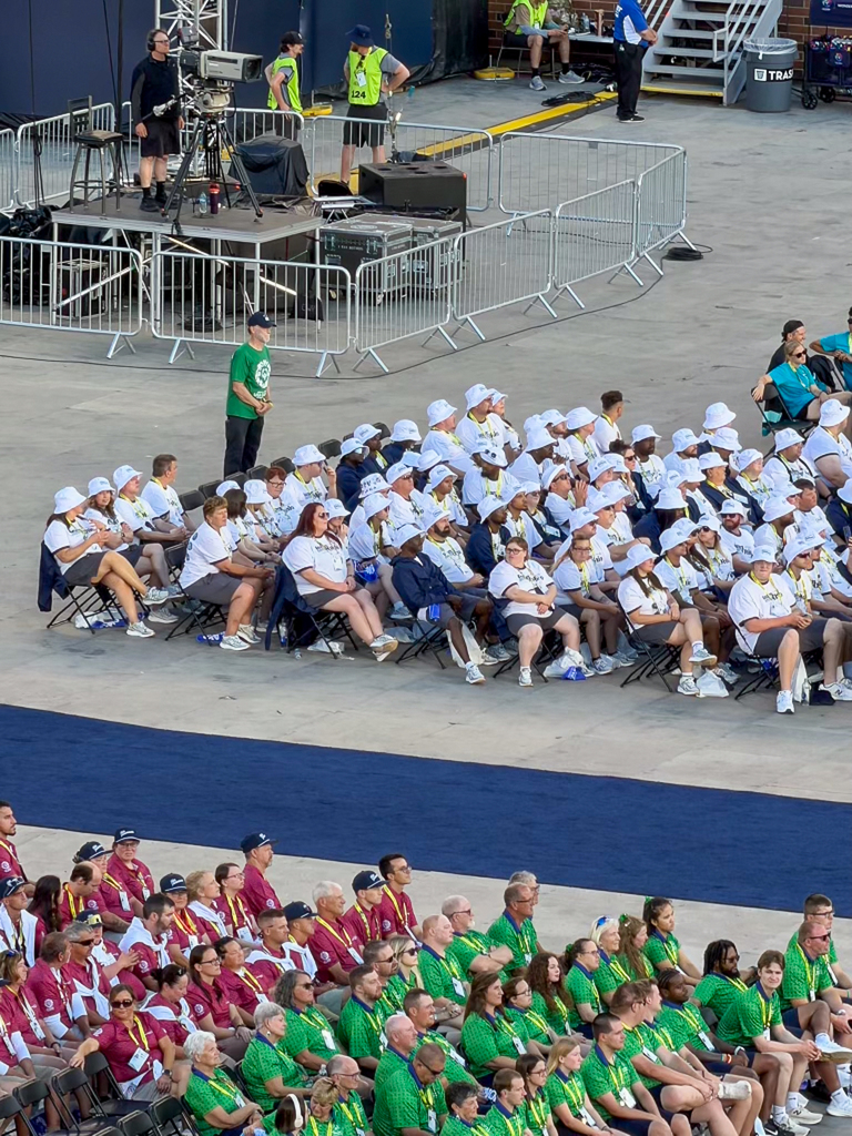 Athletes, coaches and supporters representing several Special Olympics delegations sit together during a large ceremony in an indoor stadium.