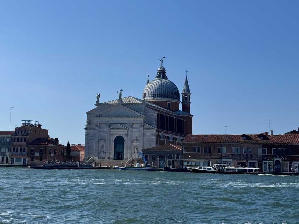 Large domed church along the waterfront in Venice, Italy, surrounded by historic buildings and boats on the lagoon.