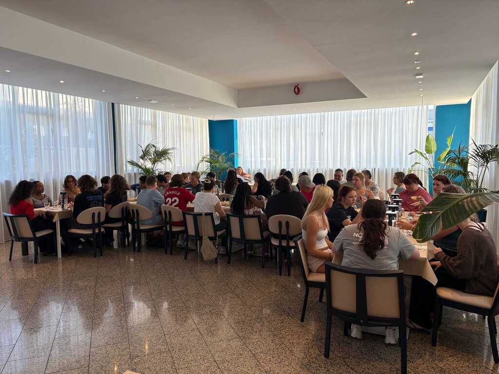 Large group of students seated together at tables inside a bright restaurant during their international trip.