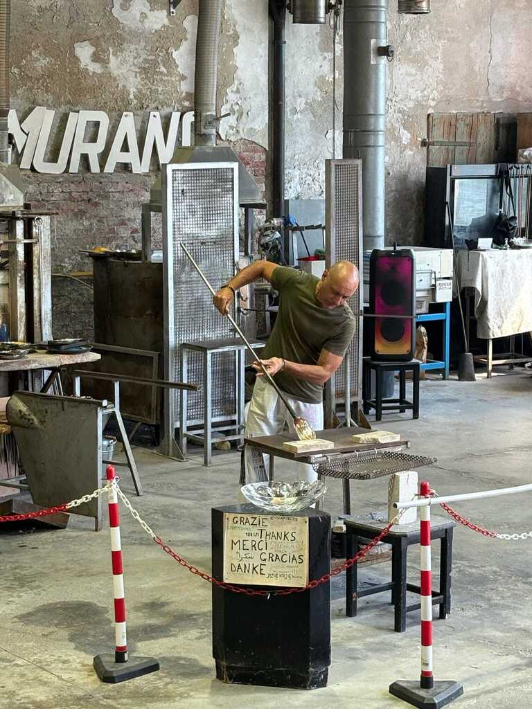 Professional glassmaker in a Murano workshop shaping molten glass with traditional tools.
