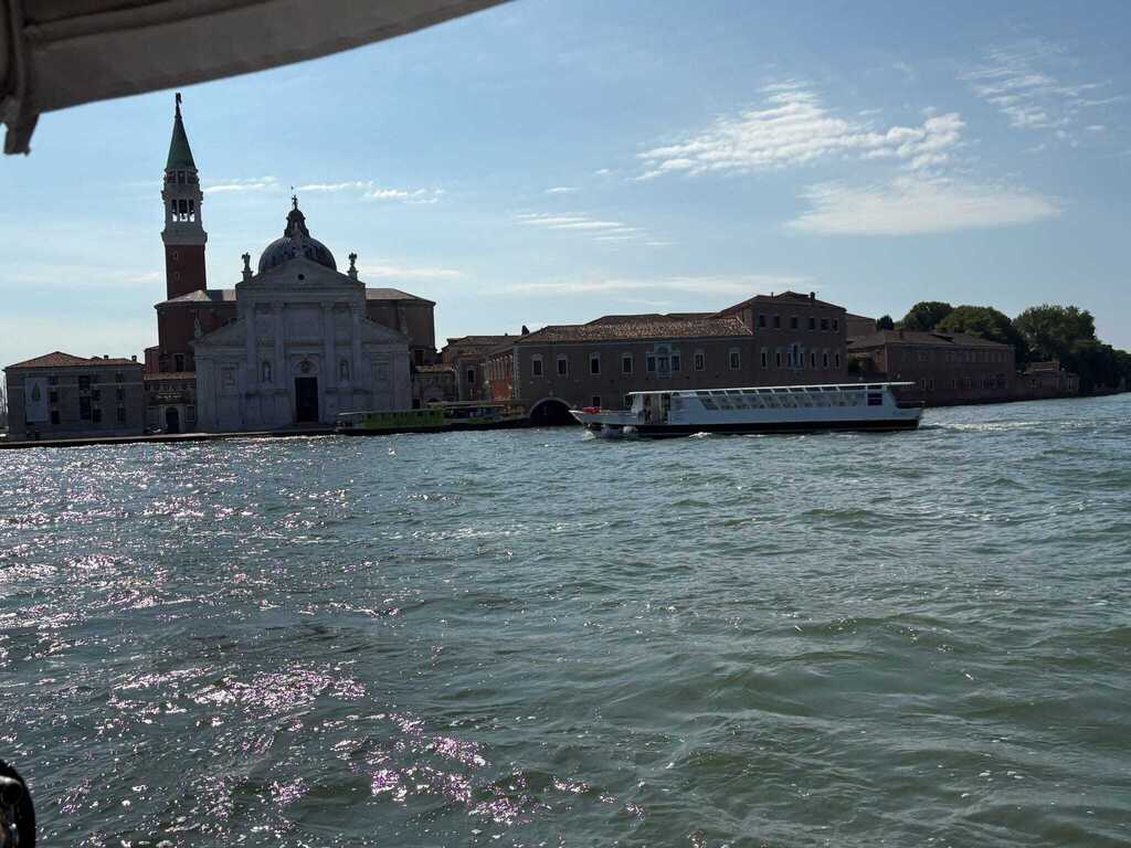 View across the Venetian Lagoon toward San Giorgio Maggiore, with its church and bell tower visible as boats travel across the water.