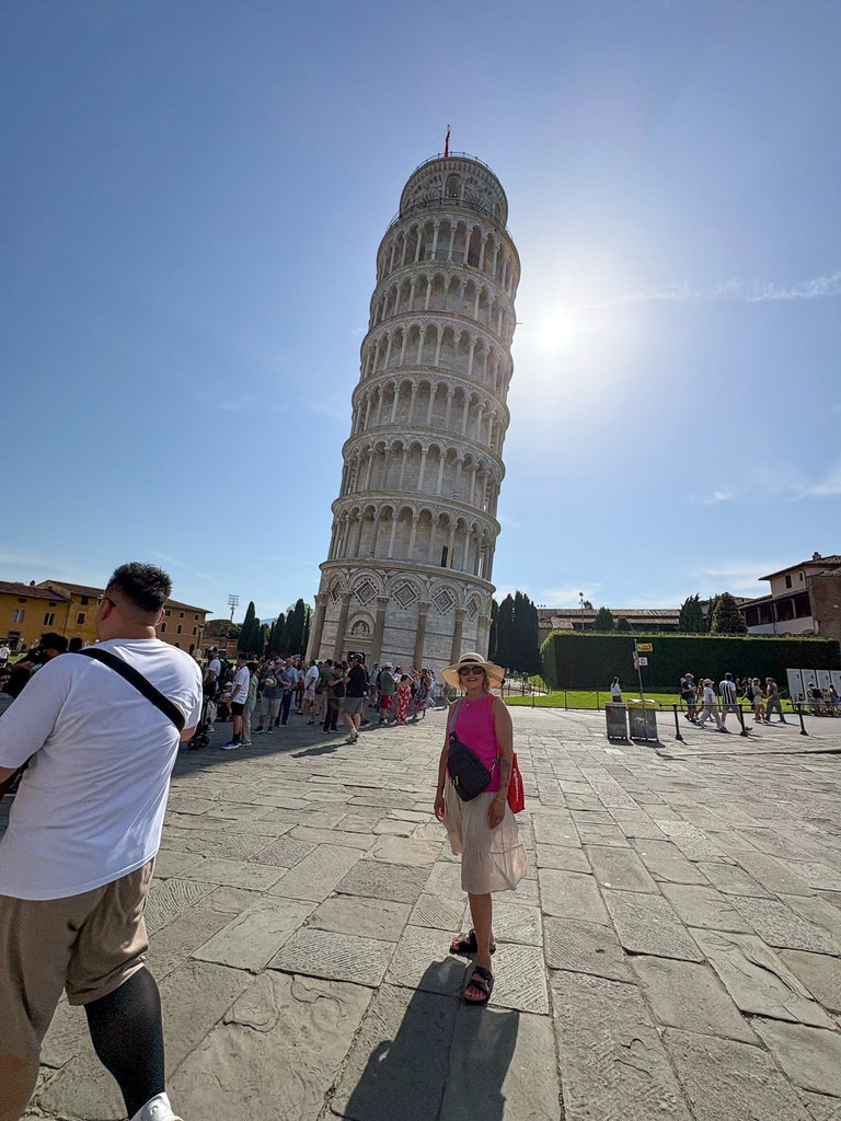 A visitor poses in front of the Leaning Tower of Pisa as sunlight shines from behind the famous landmark.