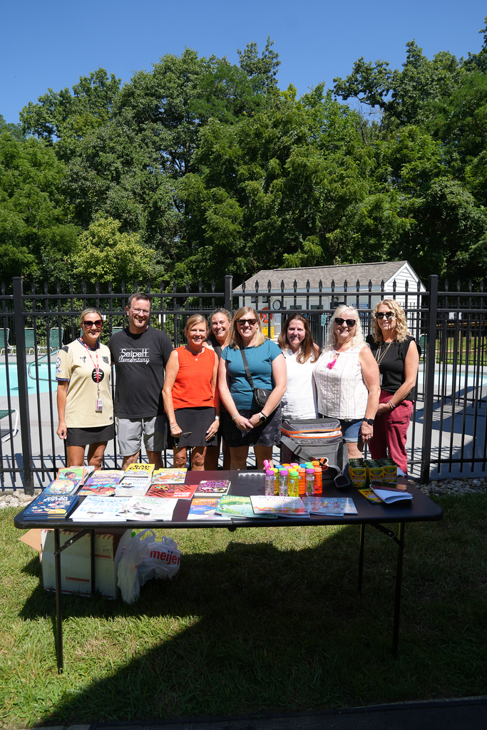 Five Seipelt Elementary staff members smile for a group photo behind a table filled with books, bubbles, crayons and other giveaways.