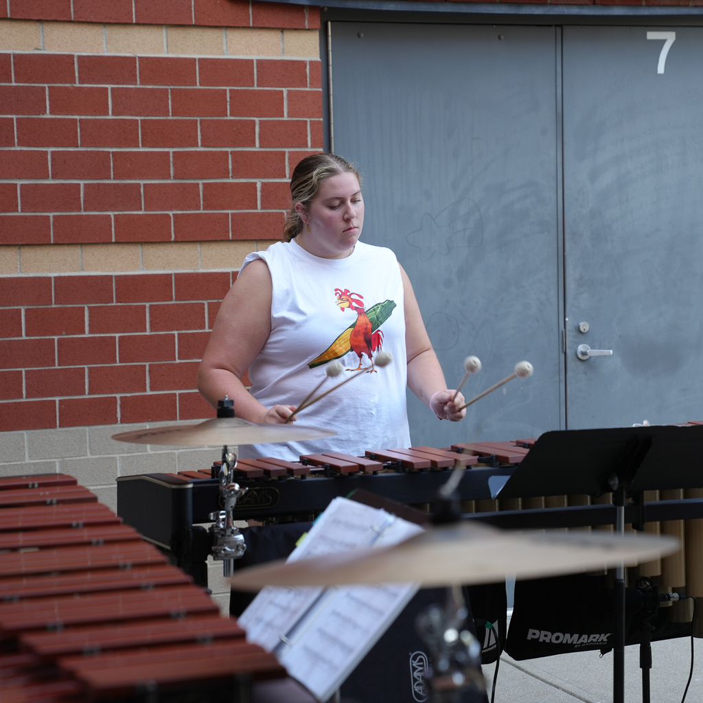 A student percussionist plays a marimba with four mallets during an outdoor Band Camp rehearsal.