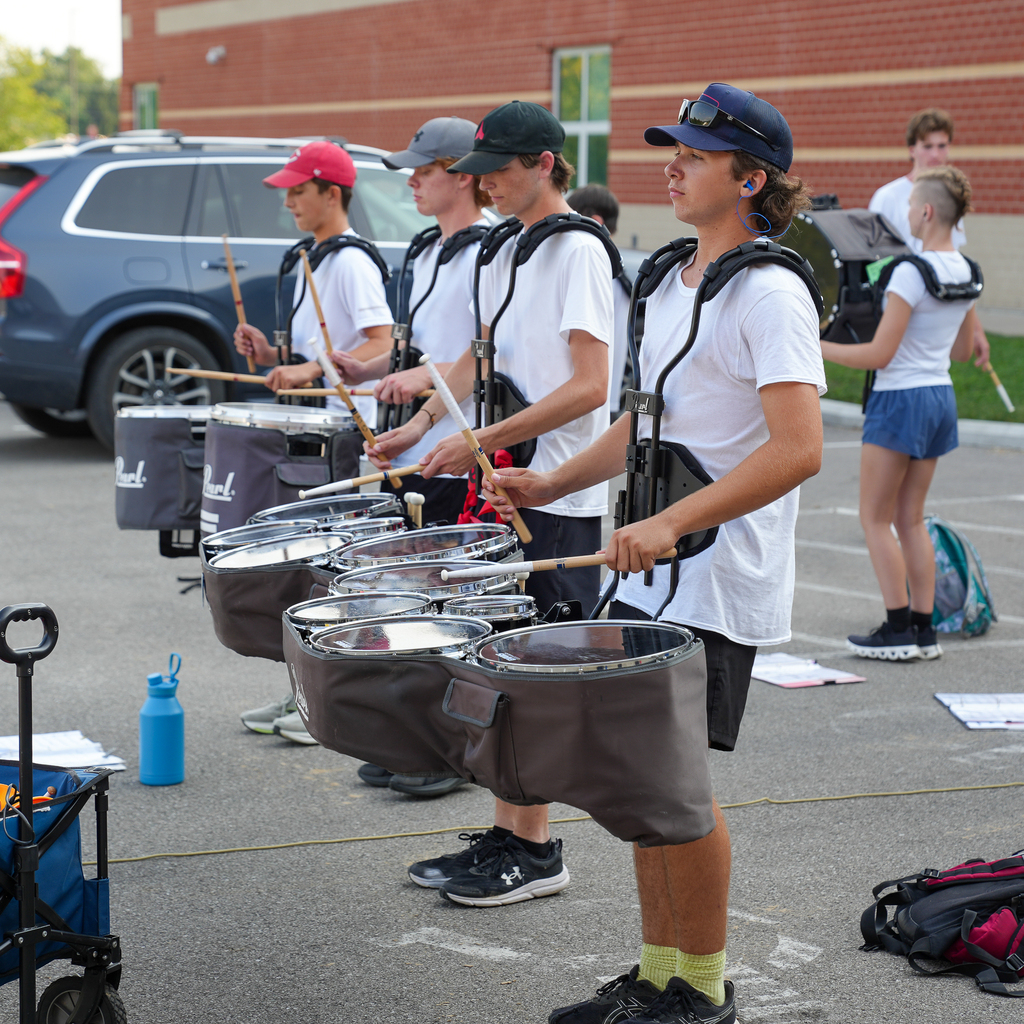 Members of the Milford drumline rehearse together outside while wearing marching tenor drums.