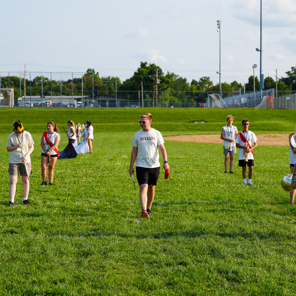 Band Director Jacob Carpenter walks through the marching band’s formation as students rehearse on a grassy field.