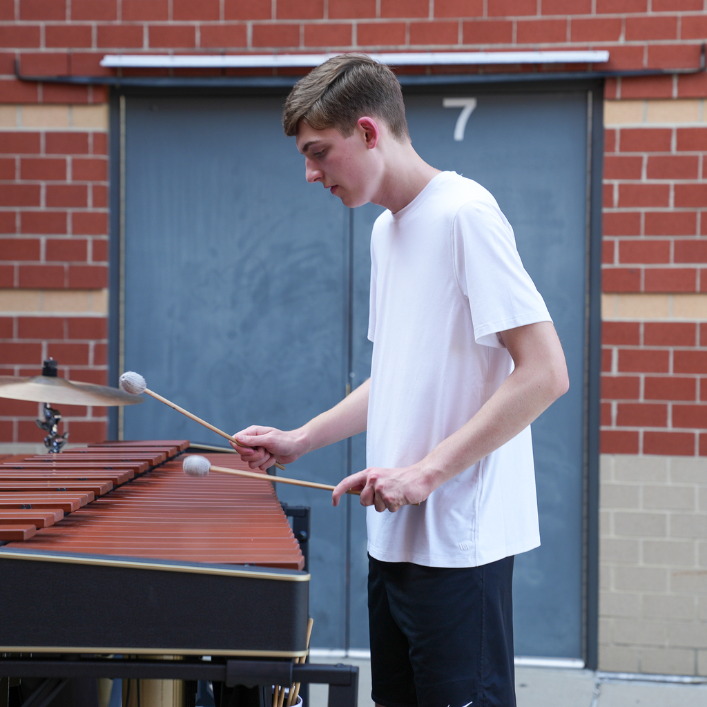 A student percussionist concentrates while playing a marimba with two mallets outside the school.
