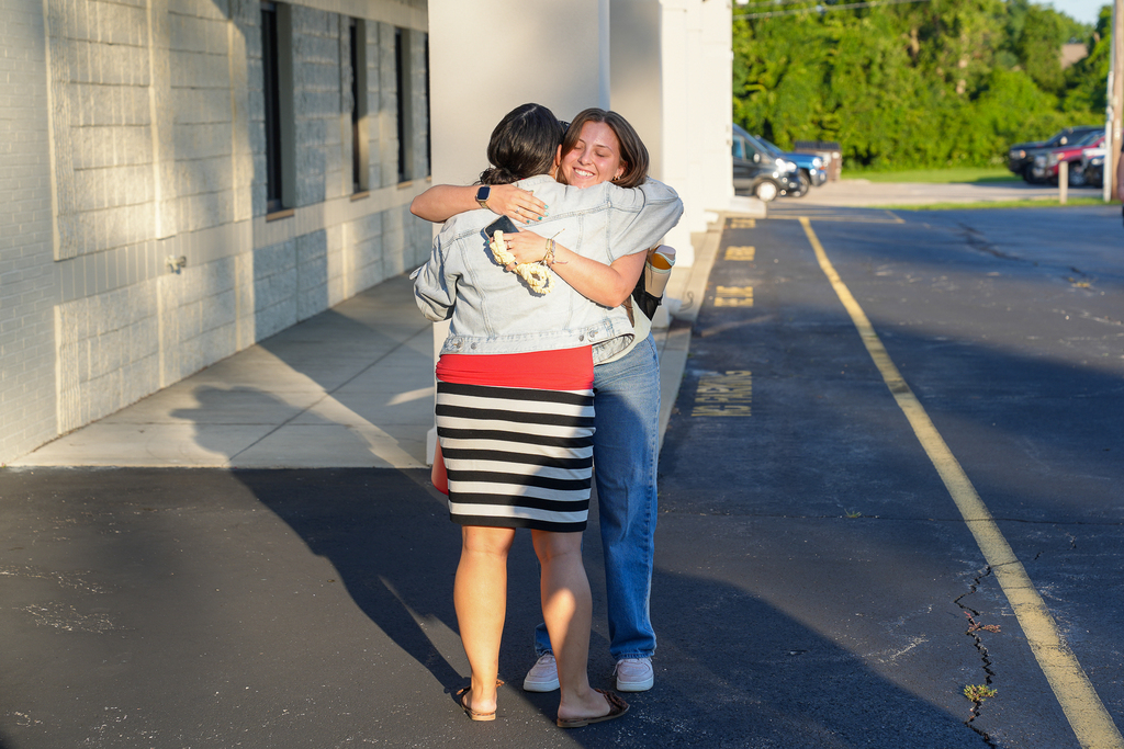 A Milford staff member embraces a smiling participant outside a school building during Milford University.