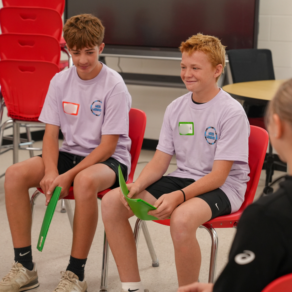 Two incoming sixth-grade students sit across from one another during a small-group icebreaker activity at Milford Middle School WEB Orientation. The students smile and engage in conversation while getting to know one another.