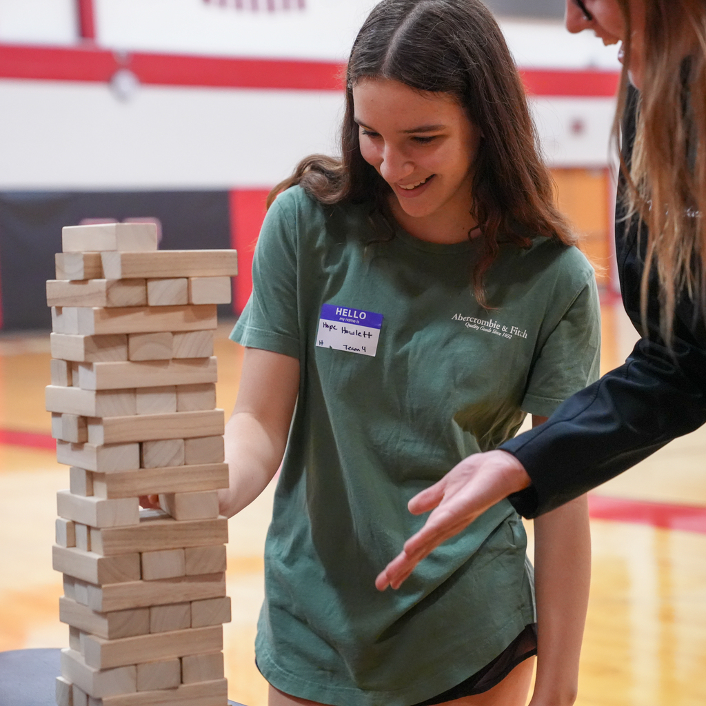 A Milford High School freshman smiles while playing a giant Jenga game during Freshman Orientation as another student offers encouragement nearby.