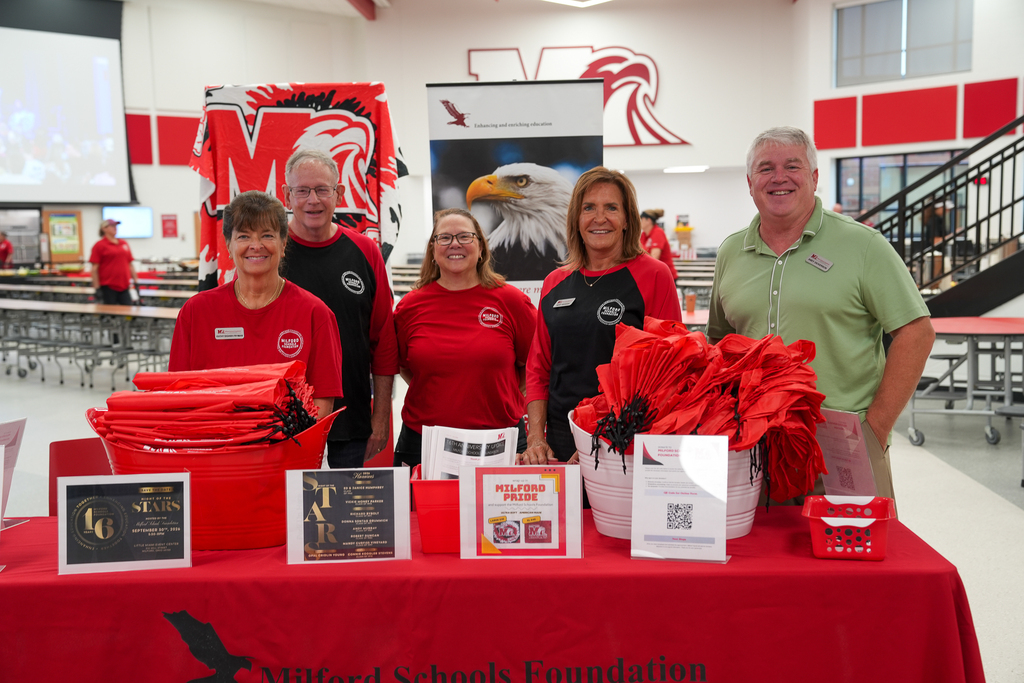 Members of the Milford Schools Foundation smile behind a display table filled with information and red Milford items during the District’s annual staff convocation.