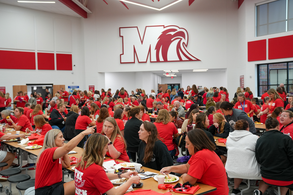 Milford Schools staff members, many dressed in red, gather around cafeteria tables for lunch during the District’s annual staff convocation.