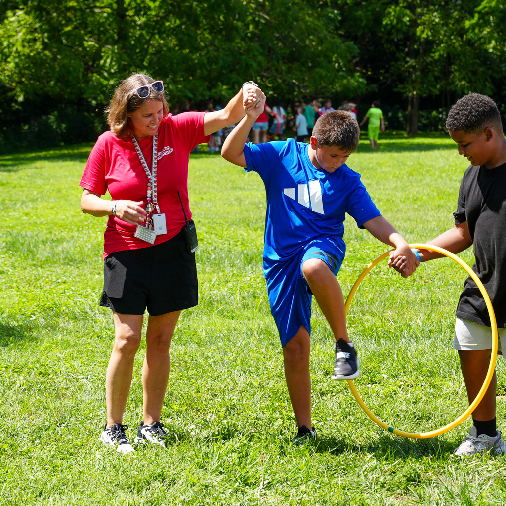 A staff member helps a McCormick Elementary student step through a hula hoop held by a classmate during a team activity.