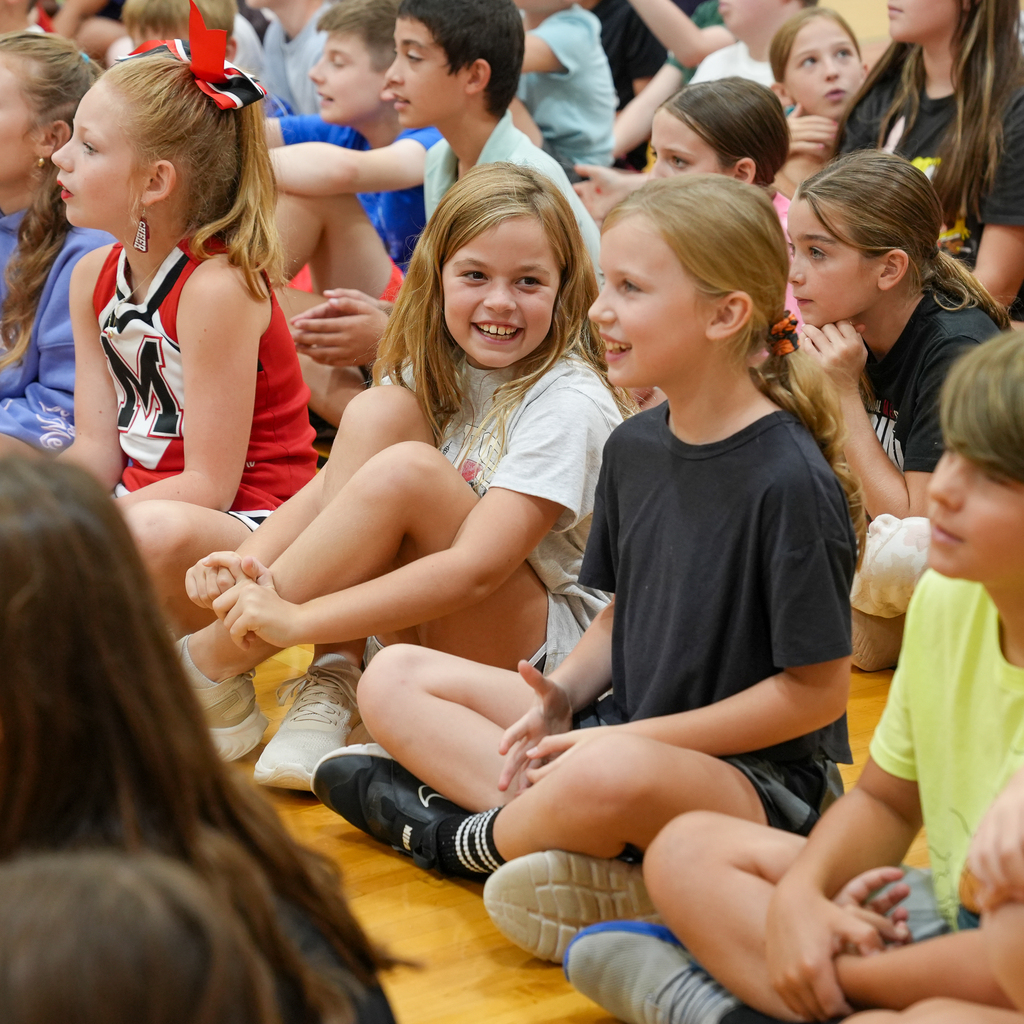Boyd E. Smith students sit together on the gym floor, smiling during a school assembly.