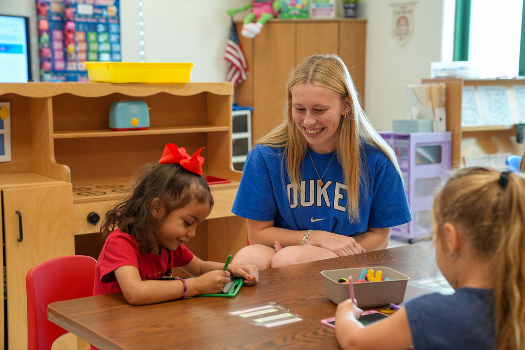 A Milford High School student mentor smiles while sitting at a classroom table with two Mulberry Elementary students as they work on an activity.