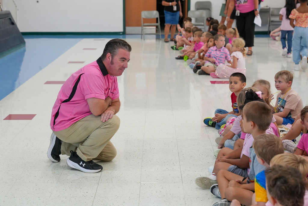 a man with slick back hair is talking with kindergarten studebnts