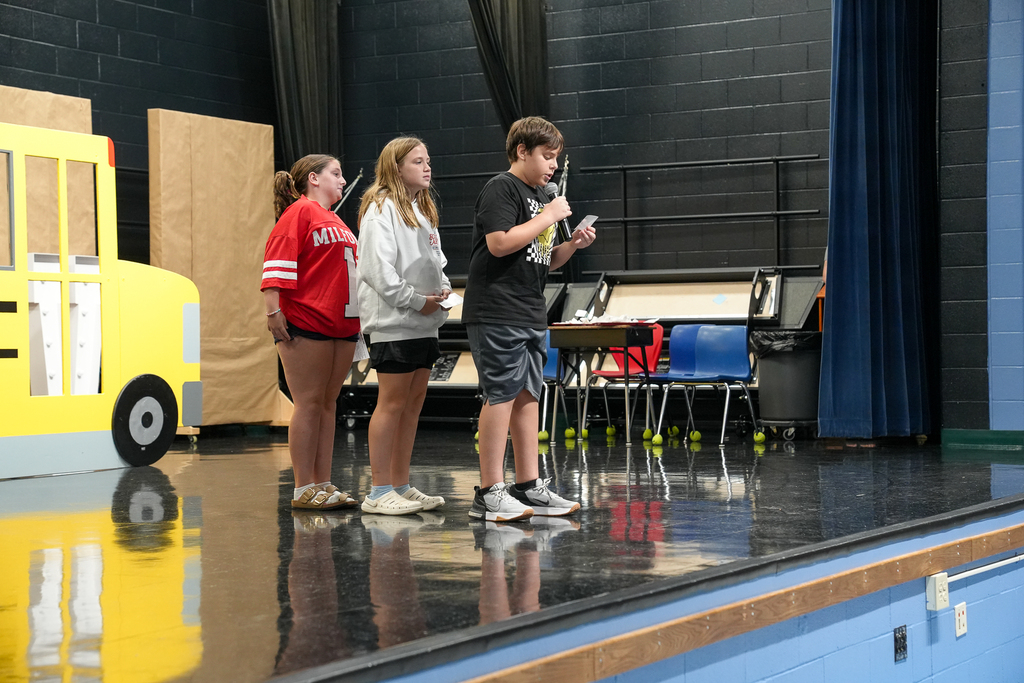 Three fifth-grade students present to younger students from the Meadowview stage.