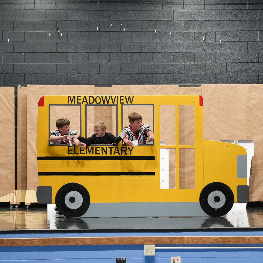 Three students perform inside a large cardboard Meadowview Elementary school bus during the assembly.
