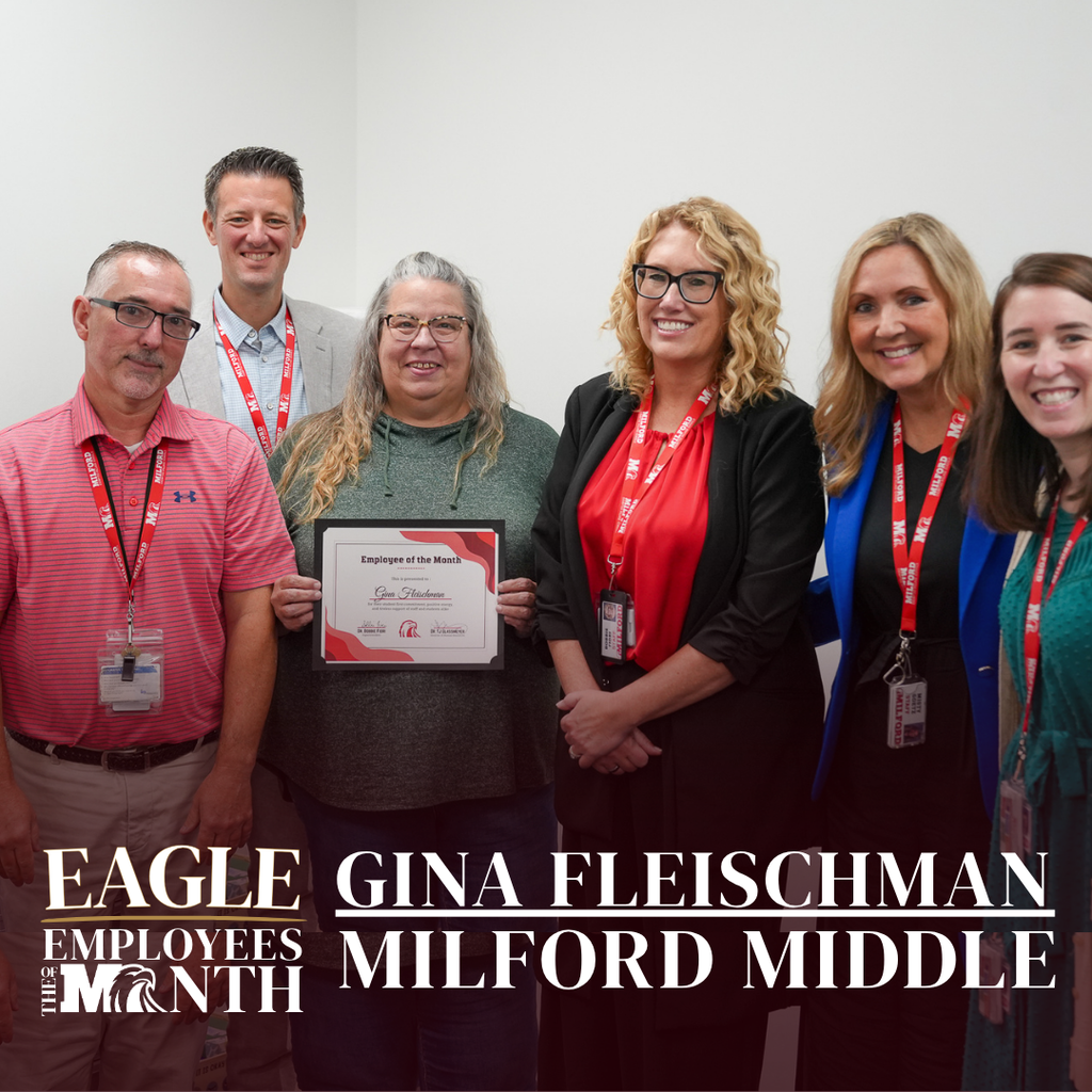Six school staff members pose indoors around Gina Fleischman, who is holding an "Employee of the Month" framed certificate. The text overlay reads: "EAGLE EMPLOYEES OF THE MONTH — GINA FLEISCHMAN — MILFORD MIDDLE".