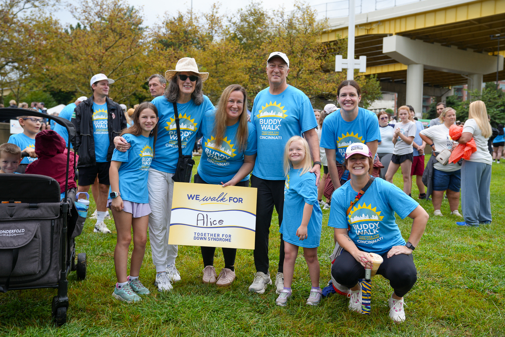 A group of Buddy Walk participants pose together on the grass during the Cincinnati event, with a large crowd gathered behind them.