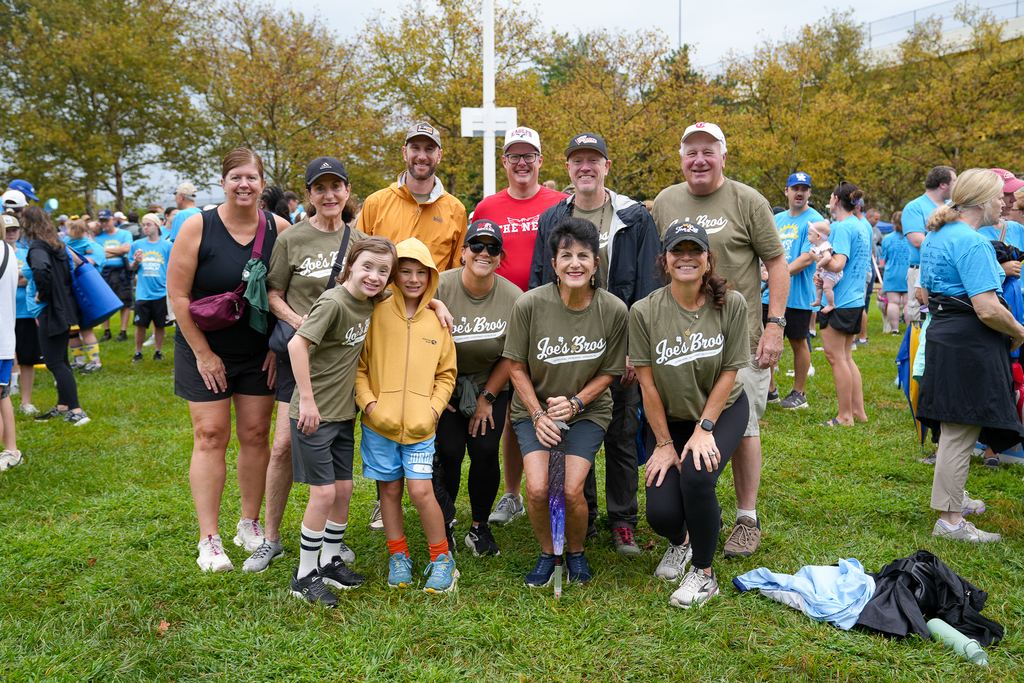 A group of Buddy Walk participants pose together on the grass during the Cincinnati event, with a large crowd gathered behind them.