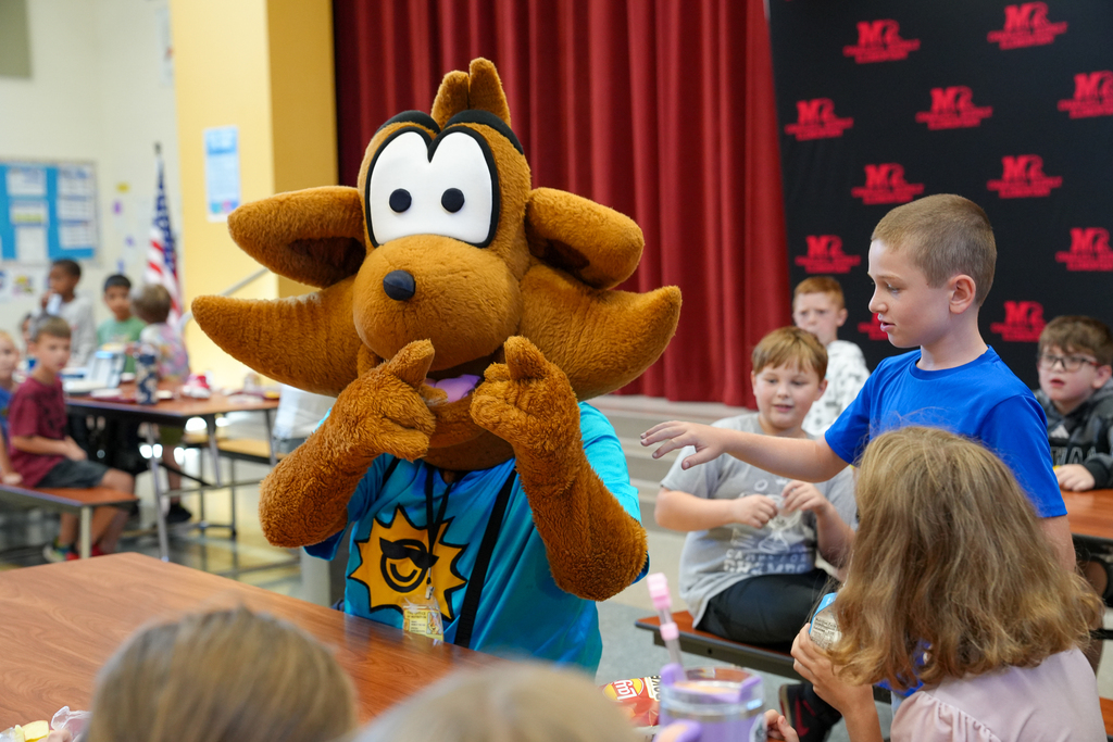 Munch the Fox interacts with students seated at cafeteria tables during lunch at Milford.