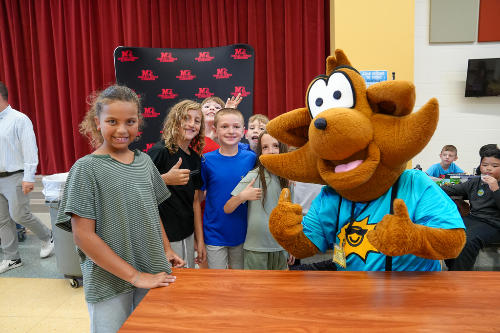 Munch the Fox poses with a group of smiling students in the school cafeteria during a visit to Milford.
