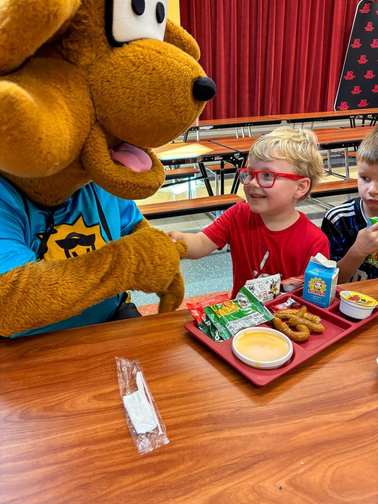 Munch the Fox greets a student at a cafeteria table as the student enjoys a school lunch.