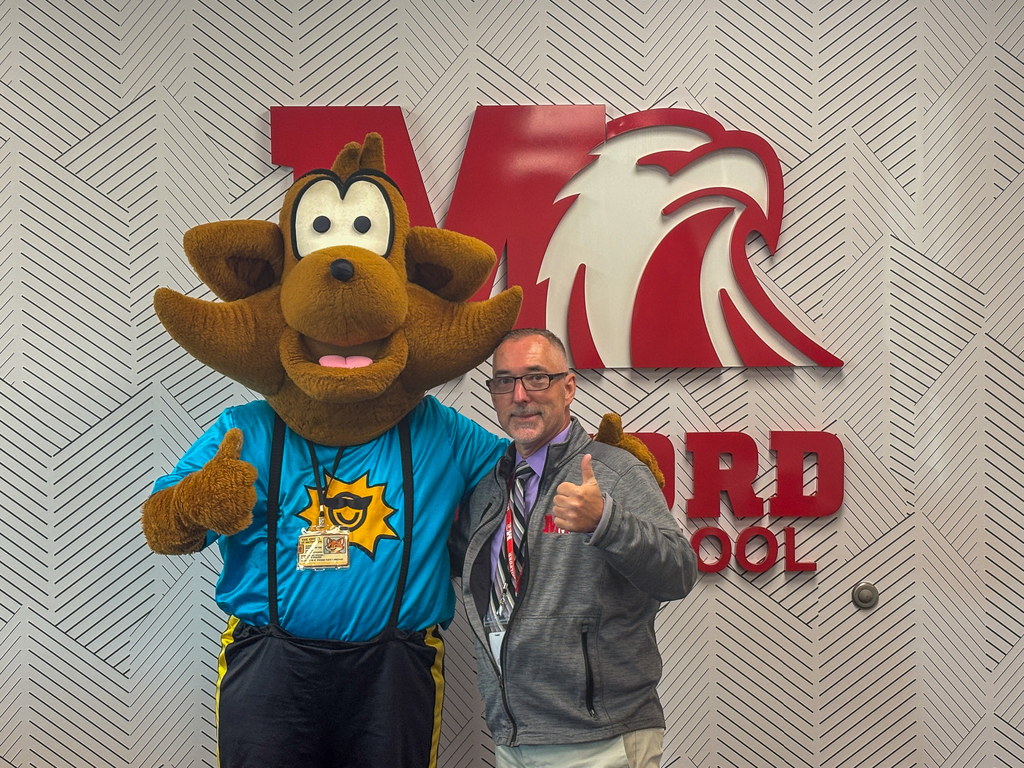 Munch the Fox and a Milford Middle School staff member give thumbs up while posing in front of the school’s Eagle logo.