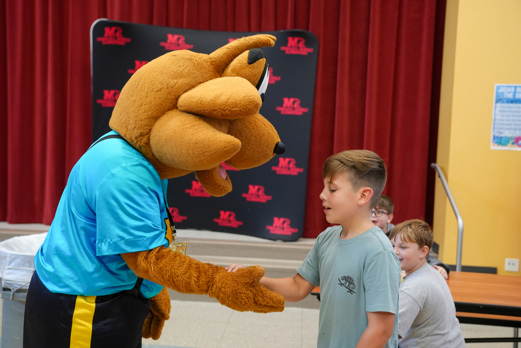Munch the Fox shakes hands with a student during lunchtime as other students look on.